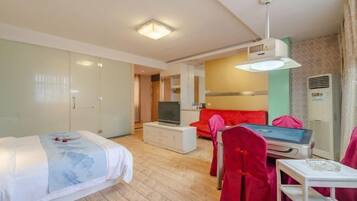 A hotel room with a bed, a TV on a white cabinet, a red sofa, and a small table with a chair.