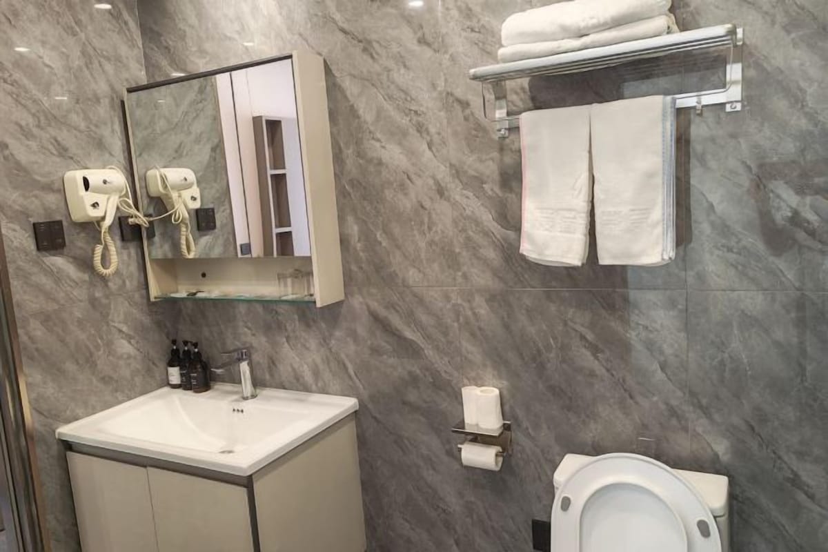 Un baño con pared de mármol, un lavabo, un espejo, un teléfono, un perchero para toallas y un inodoro.