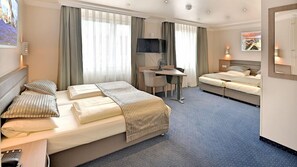 Une chambre d’hôtel avec un lit, un bureau, un deuxième lit et un téléviseur.