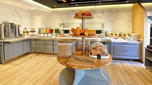 Un buffet de petit-déjeuner avec un assortiment de fruits, des machines à café et une variété de plats.
