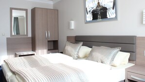 A modern bedroom with a large bed, a wardrobe, a bedside table, and a wall-mounted TV displaying a cathedral interior. - St. Joseph Hotel (Hamburg)
