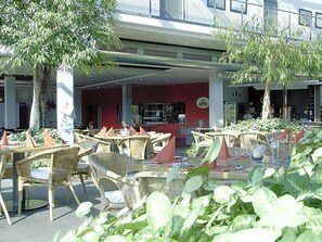 Ett utomhusområde med sittplatser, bestående av bord och stolar i rotting, en röd vägg och en byggnad i bakgrunden.