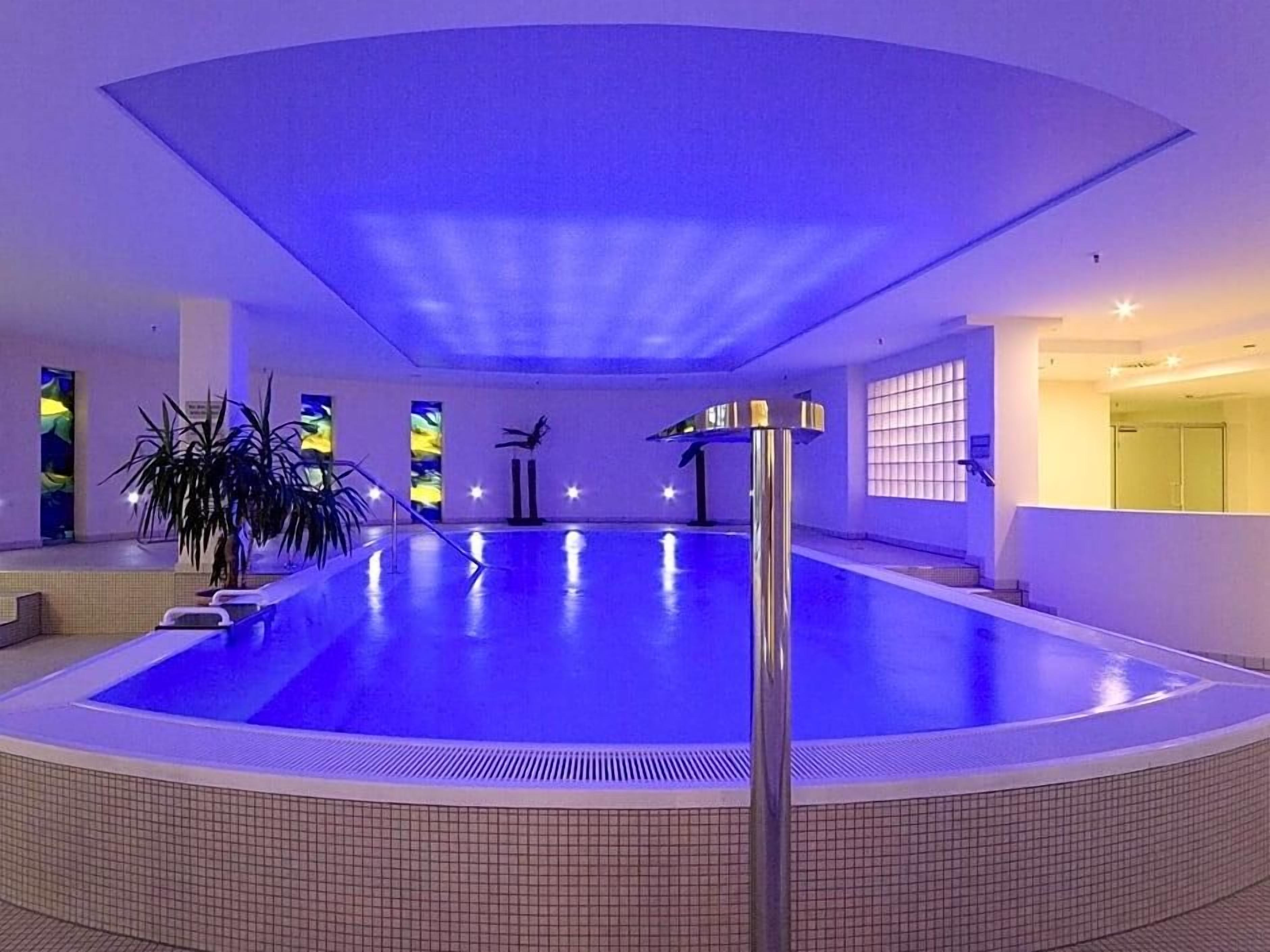 An indoor swimming pool with a tiled floor, a central pole, and a potted plant.