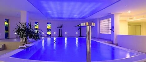 An indoor swimming pool with a tiled floor, a central pole, and a potted plant.