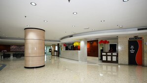 Un hall d’hôtel comprenant un comptoir d’accueil, une grande colonne cylindrique et un panneau indiquant le rez-de-chaussée.