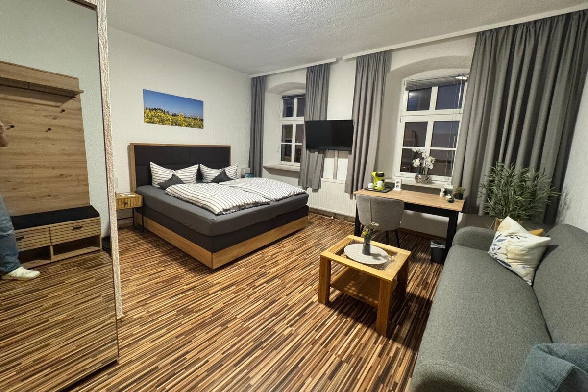 Quarto moderno com cama, mesa de cabeceira, escrivaninha e sofá cinza.