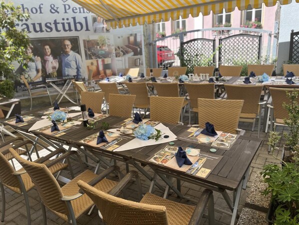 Un área de comedor al aire libre con sillas y mesas de mimbre, algunas con individuales y servilletas.