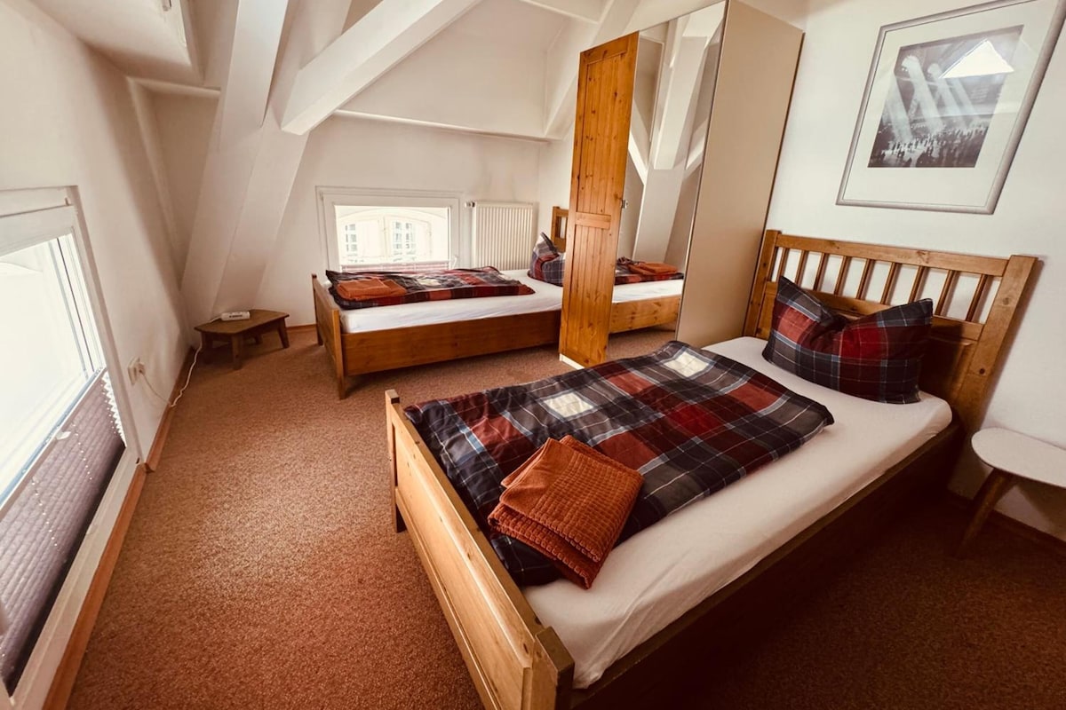 Quarto com duas camas de madeira, uma janela, radiador e um quadro na parede.
