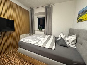 Un dormitorio moderno con cama, televisión, ventana con cortinas y un cuadro en la pared.