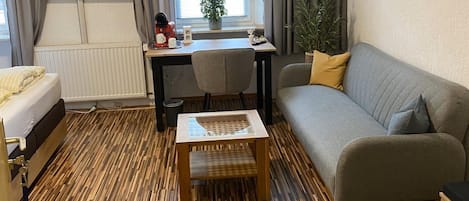 A modern living room with a sofa, a coffee table, a desk with a computer, a TV mounted on the wall, and a window with curtains.