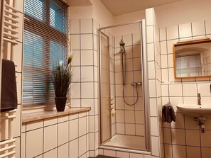 A bathroom with a shower, a sink, and a window with blinds.