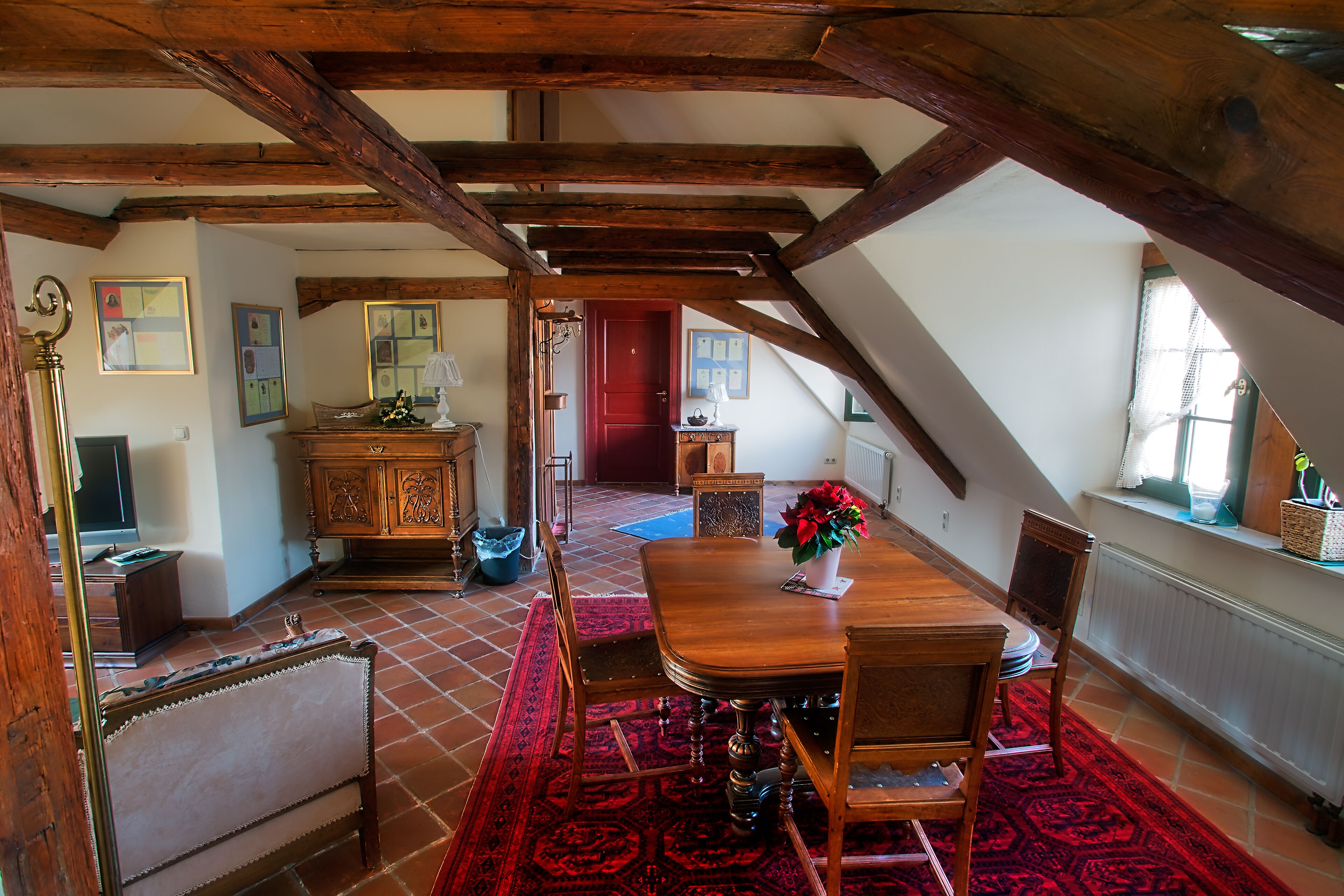 Un comedor con una mesa de madera, sillas y una alfombra roja. Se observa una ventana con vistas al exterior.