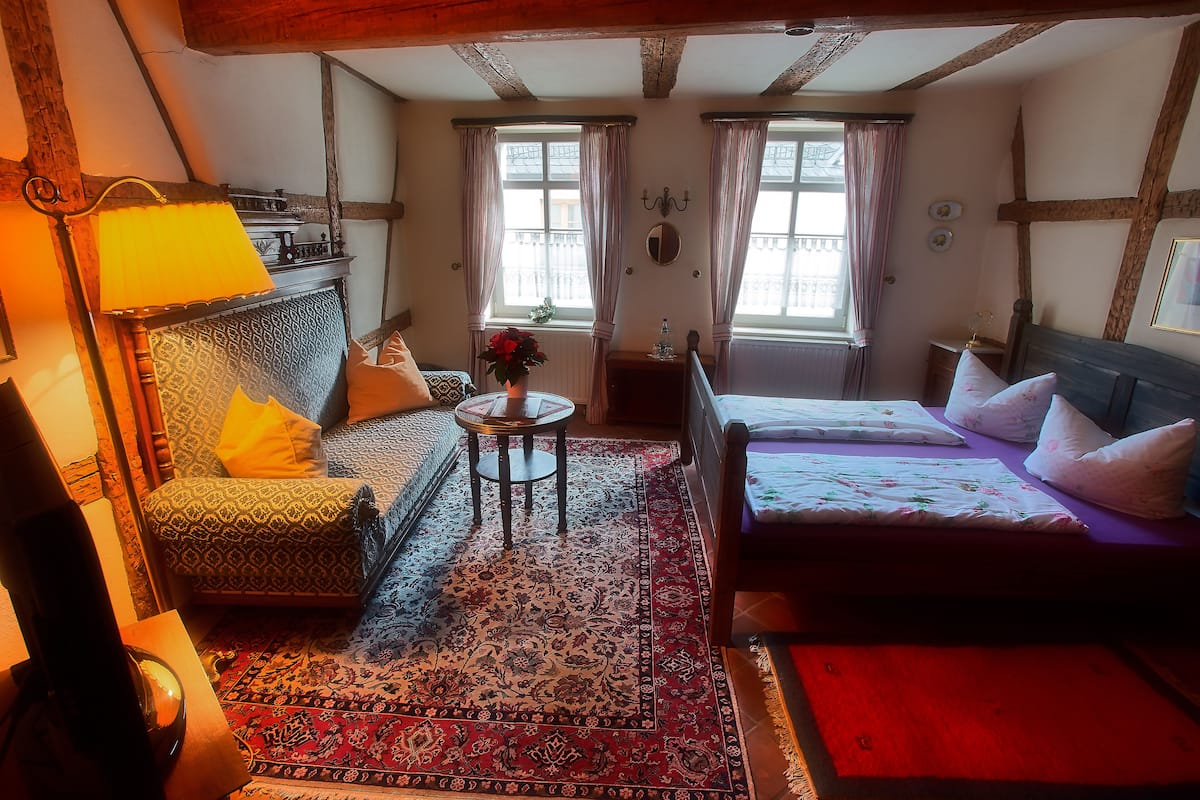 Una habitación tradicional con sofá, cama, una mesita con un florero y chimenea.