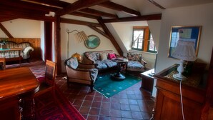 A room with a wooden ceiling, a sofa set, a dining table, and a lamp.