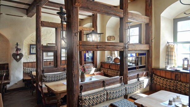 A rustic interior with wooden beams, checkered benches, and a cozy dining area.