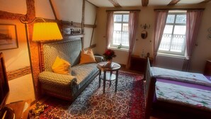 A cozy room with a patterned sofa, a small round table, a bed with floral bedding, and a window with curtains.