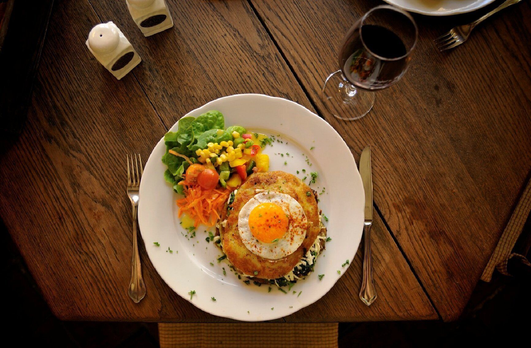 A plate with a fried egg, vegetables, and a side salad on a wooden table.