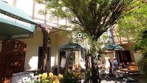 An outdoor cafe area with tables and chairs, potted plants, and umbrellas.