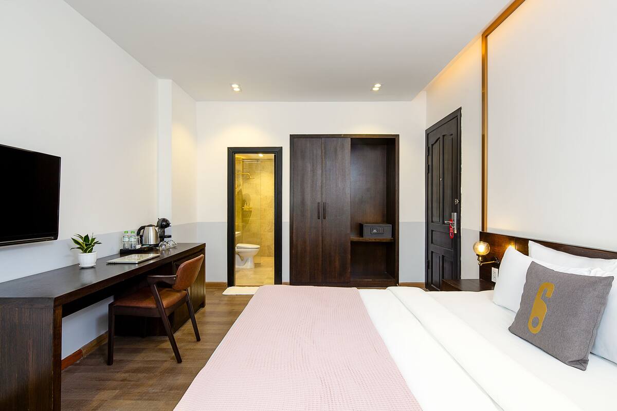 Una habitación de hotel moderna con cama, escritorio, silla, televisor y armario.