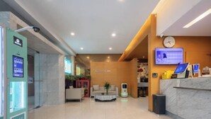 Eine Hotellobby mit einer Rezeption, einer Uhr, einem Fernseher und einem Automaten.