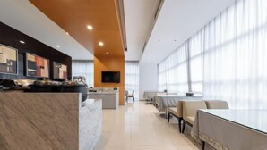 Eine moderne Hotelhalle mit einem Marmor-Rezeptionstresen, einem Flachbildfernseher und einem Essbereich mit Tischen und Stühlen.