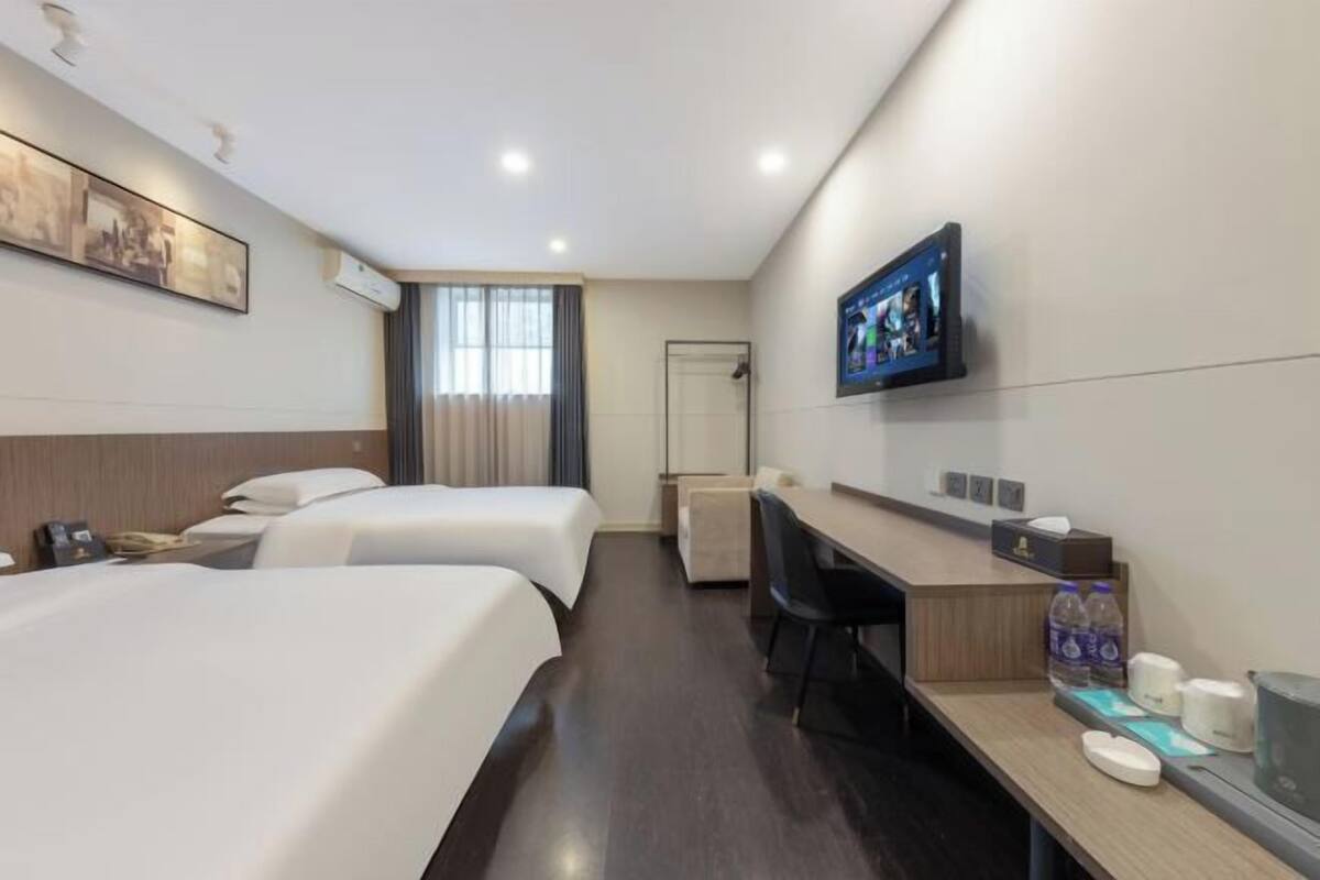 Une chambre d’hôtel avec deux lits, un bureau, une télévision et une fenêtre avec des rideaux.