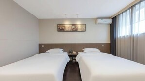 Ein Hotelzimmer mit zwei Einzelbetten, einem kleinen Tisch, einer Wand-Klimaanlage und einem Bild über dem Bett.