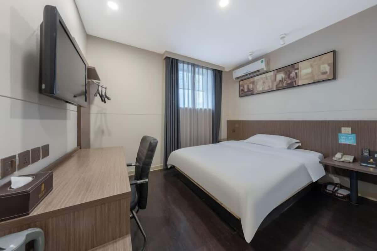 Une chambre d’hôtel équipée d’un lit, d’un bureau, d’une chaise, d’une télévision et d’œuvres d’art accrochées au mur.