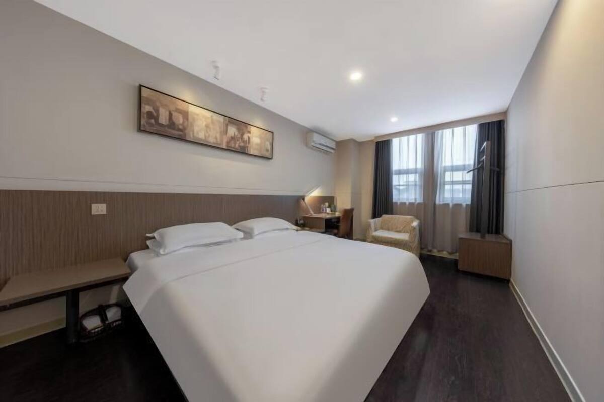 Une chambre d’hôtel avec un grand lit, un bureau, une chaise, un tableau au mur et une fenêtre avec des rideaux.
