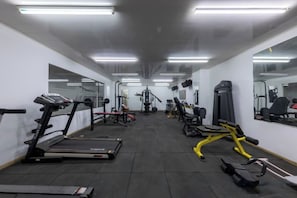 Un gimnasio con cintas de correr, máquinas de pesas y espejos en las paredes.