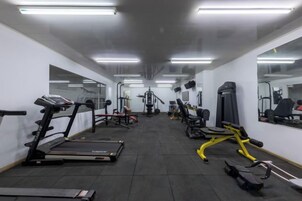 Un gimnasio con cintas de correr, máquinas de pesas y espejos en las paredes.
