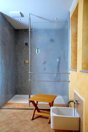 Un baño moderno con cabina de ducha de vidrio, un taburete de madera y un lavamanos blanco.