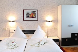 Habitación de hotel con una cama doble, dos mesitas de noche, un armario y un cuadro enmarcado en la pared.