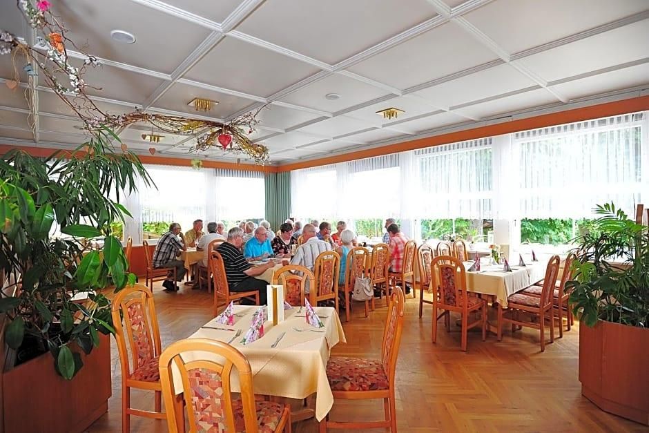 Un espace repas comprenant plusieurs tables et chaises, de grandes fenêtres et des plantes d’intérieur.
