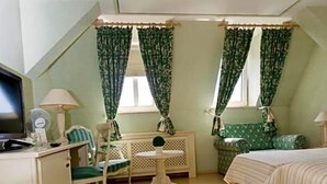 Um quarto com cama, escrivaninha, cadeira, mesa pequena e radiador.
