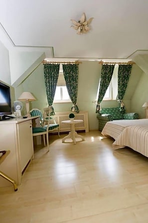 A room with a bed, a desk, a chair, a small table, and a radiator.