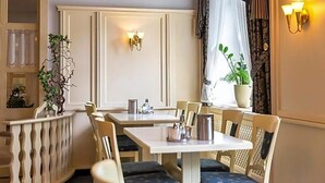 Uma sala de jantar com mesas e cadeiras, um vaso de planta e iluminação na parede.