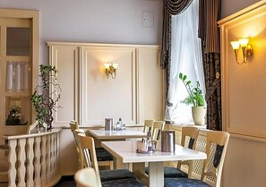 Un comedor con mesas y sillas, una planta en maceta e iluminación en la pared.