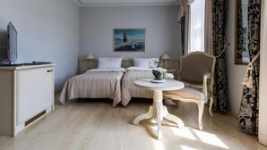 A hotel room with a bed, a chair, a table, a television, and a painting on the wall. - Burghof (Hof)