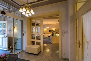 Un vestíbulo de hotel con mostrador de recepción, zona de estar y puerta de cristal que da a un comedor.