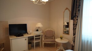 A hotel room with a bed, a desk with a television, a chair, a small table with a lamp, and a mirror. - Burghof (Hof)