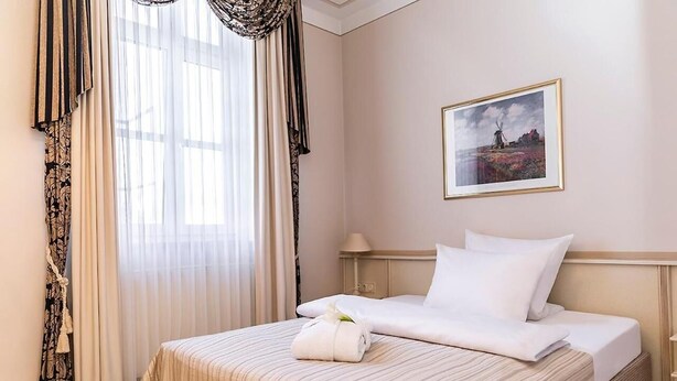 A hotel room with a bed, a framed picture on the wall, and a window with curtains. - Burghof (Hof)