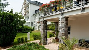 Un hotel con fachada de piedra, un espacio al aire libre cubierto con plantas y un balcón con flores rojas.