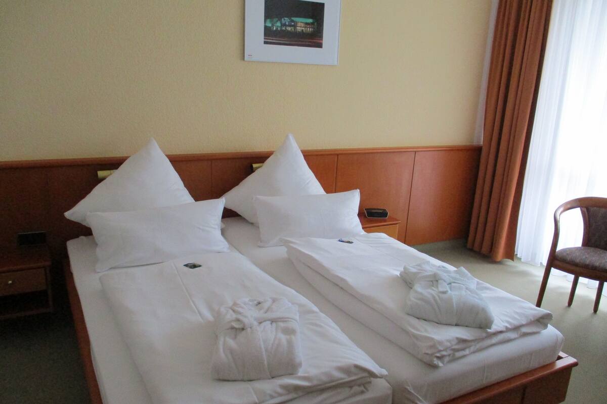 Ein Hotelzimmer mit zwei Einzelbetten, jeweils mit weißer Bettwäsche und Kissen, einem Holzkopfende, einem kleinen Nachttisch und einem Stuhl.
