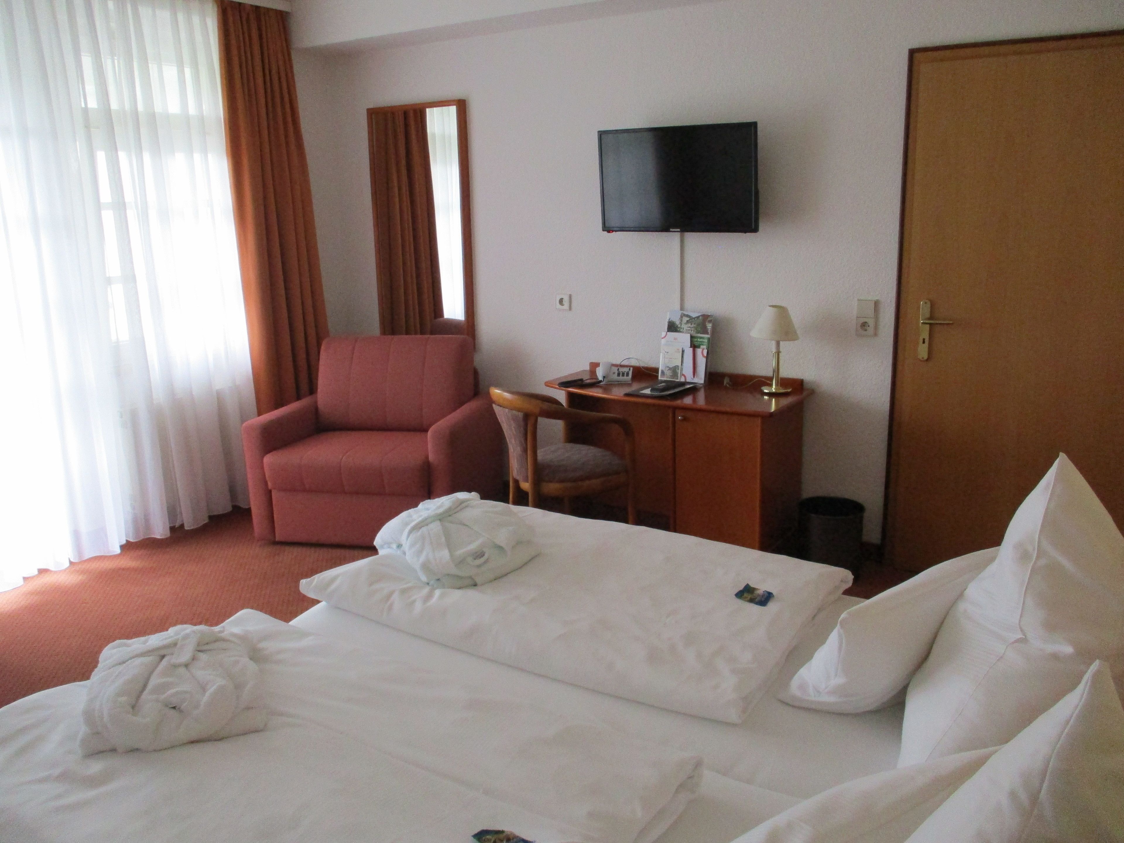 Una habitación de hotel con cama, escritorio, silla, televisor y puerta.