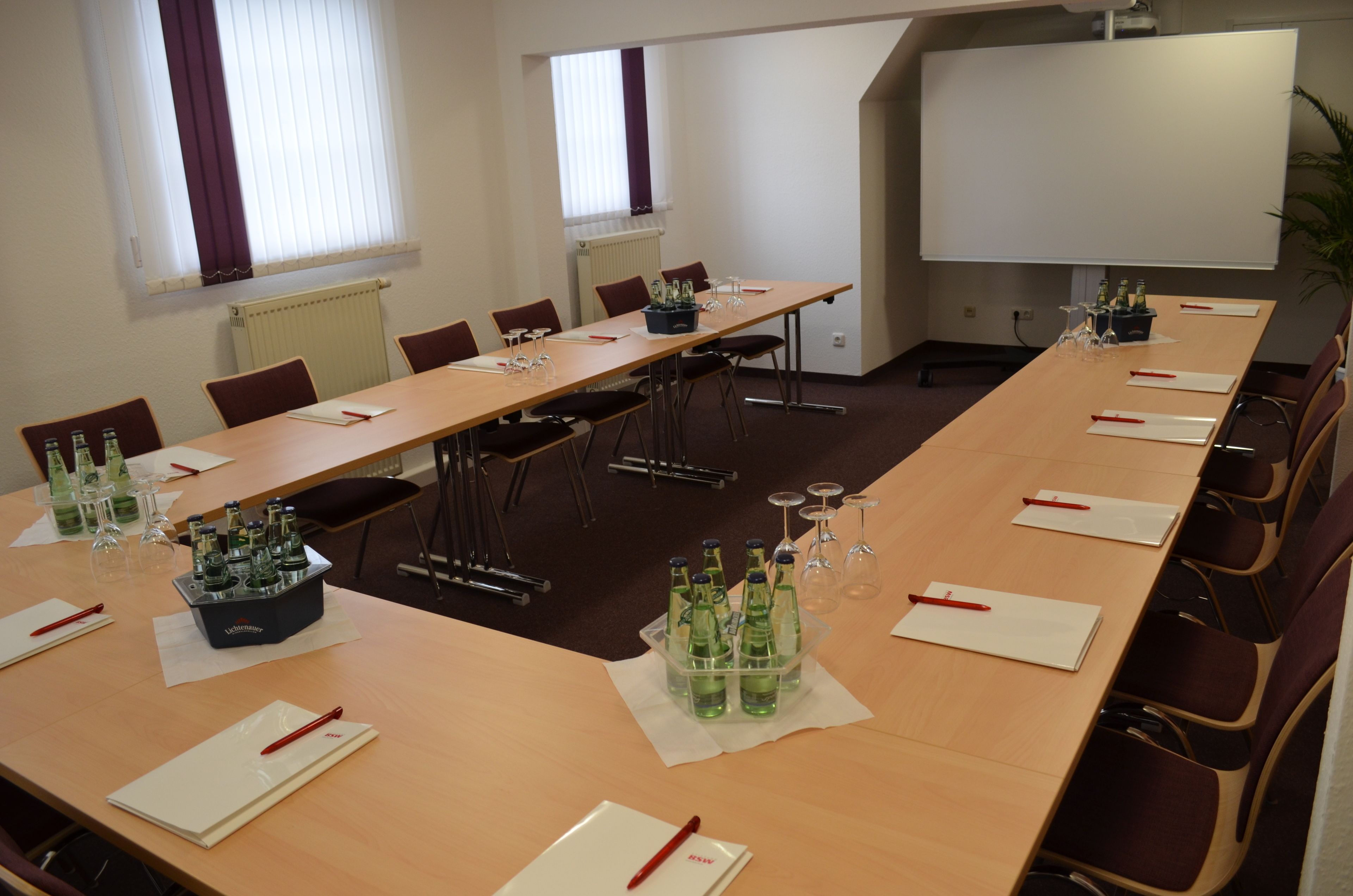 A conference room with a long table, chairs, a projector screen, and bottles of water.