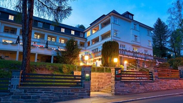 Un hotel de varios pisos con una entrada de piedra, mesas al aire libre y una fachada bien iluminada.