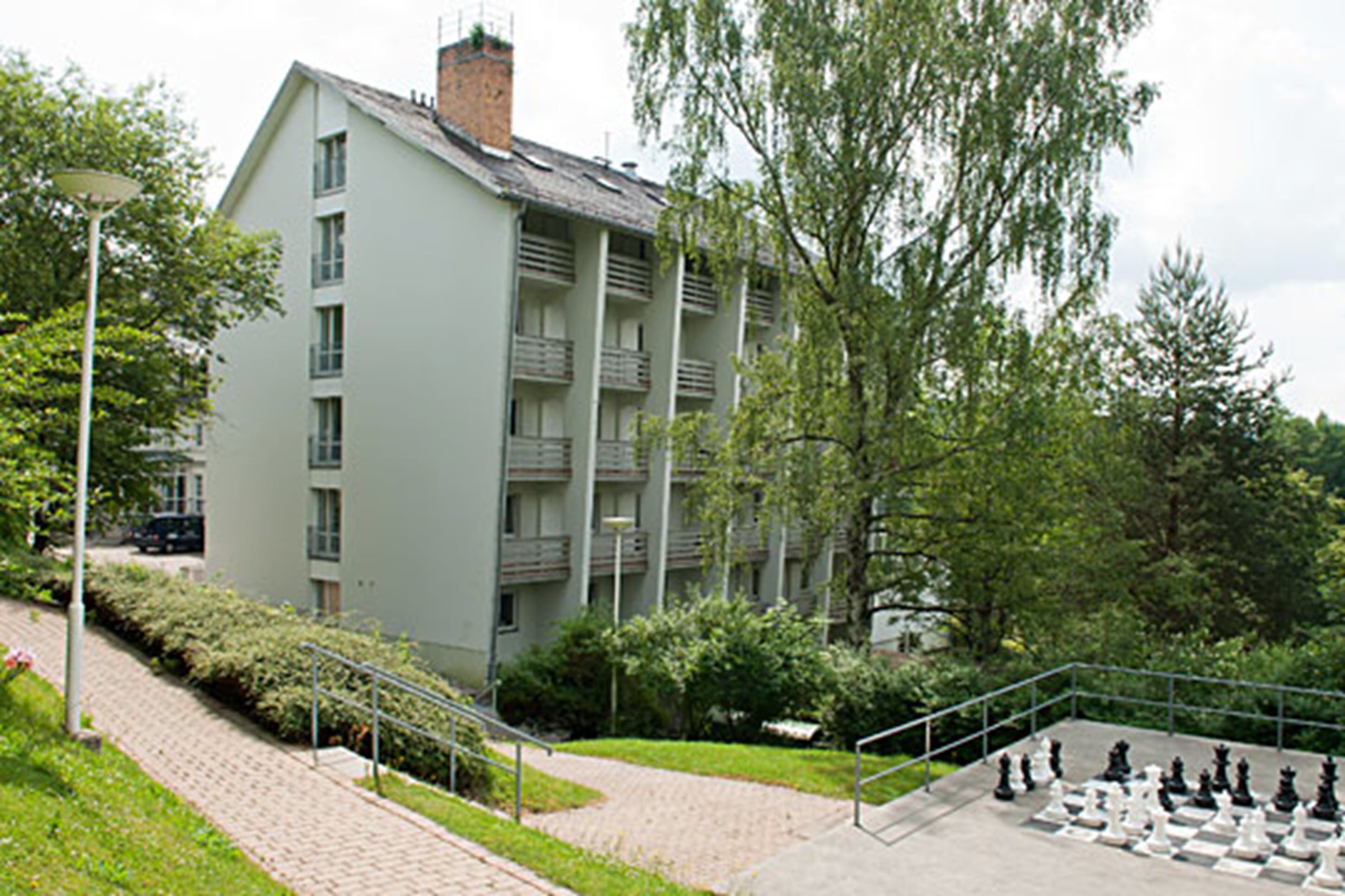 Ein mehrstöckiges Gebäude mit Balkonen, umgeben von Grünflächen und einem Schachbrett.