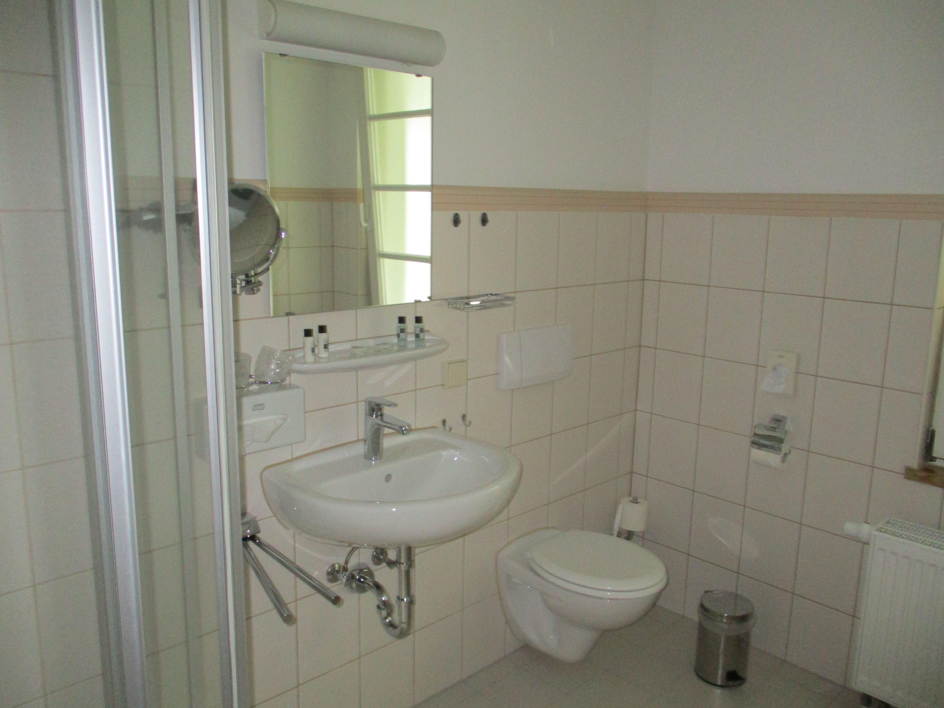 Une salle de bain équipée d’un lavabo, d’un miroir, de toilettes et d’une poubelle.