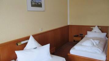 Ein Hotelzimmer mit zwei Einzelbetten, Holz-Kopfteilen, einem kleinen Nachttisch und einem gerahmten Bild an der Wand.